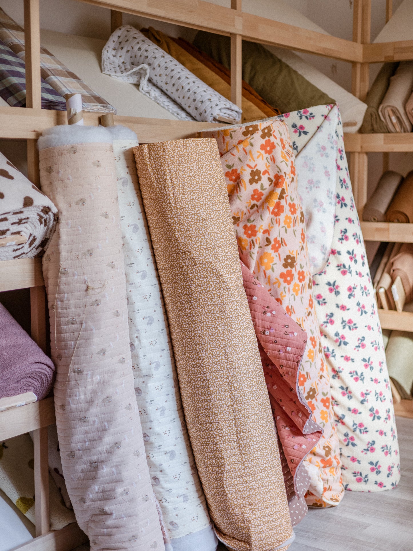 Rolls of fabric on a wooden shelf with various patterns and colors.